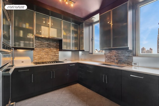 kitchen featuring dark cabinetry, light tile patterned floors, decorative backsplash, and a sink