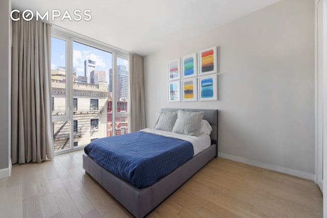 bedroom with a view of city, baseboards, floor to ceiling windows, and light wood-style floors