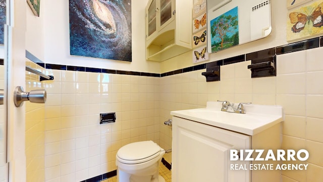 bathroom with vanity, a wainscoted wall, toilet, and tile walls