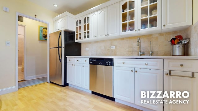 kitchen with light wood-style floors, appliances with stainless steel finishes, tasteful backsplash, glass insert cabinets, and white cabinetry