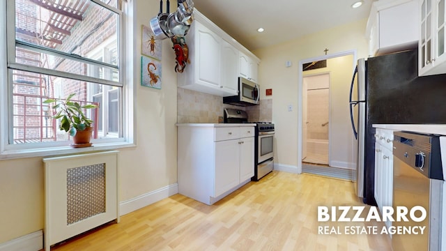 kitchen with white cabinets, appliances with stainless steel finishes, glass insert cabinets, and light wood-style flooring