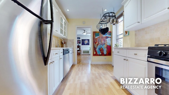 kitchen featuring light countertops, white cabinets, light wood-style flooring, appliances with stainless steel finishes, and backsplash