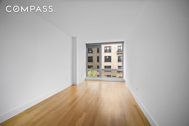 empty room featuring baseboards, a wall of windows, and light wood finished floors