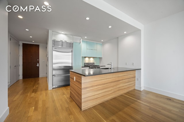 kitchen with range, dark countertops, a sink, a peninsula, and stainless steel built in refrigerator