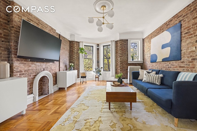 living area featuring radiator, a brick fireplace, brick wall, and a notable chandelier