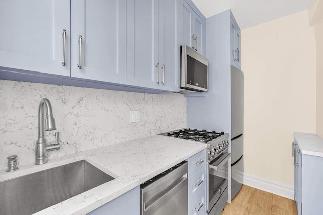 kitchen featuring a sink, decorative backsplash, appliances with stainless steel finishes, and light stone countertops