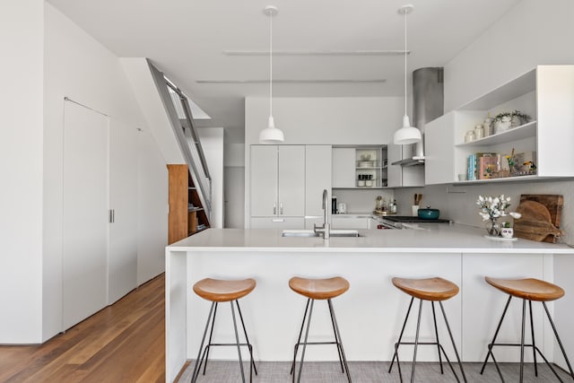 kitchen with exhaust hood, open shelves, a sink, light wood finished floors, and a peninsula