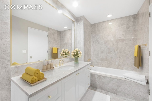 full bath with tile walls, tile patterned floors, a tub with marble appearance, and vanity