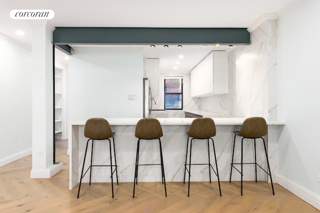 kitchen with a kitchen breakfast bar, light countertops, a peninsula, stainless steel fridge, and white cabinetry