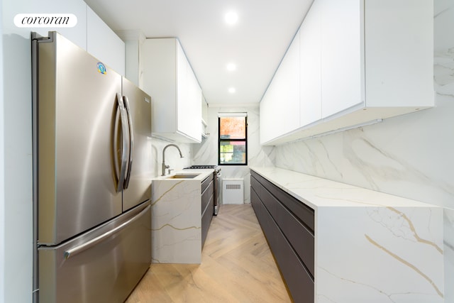 kitchen featuring modern cabinets, a sink, light stone counters, white cabinets, and freestanding refrigerator