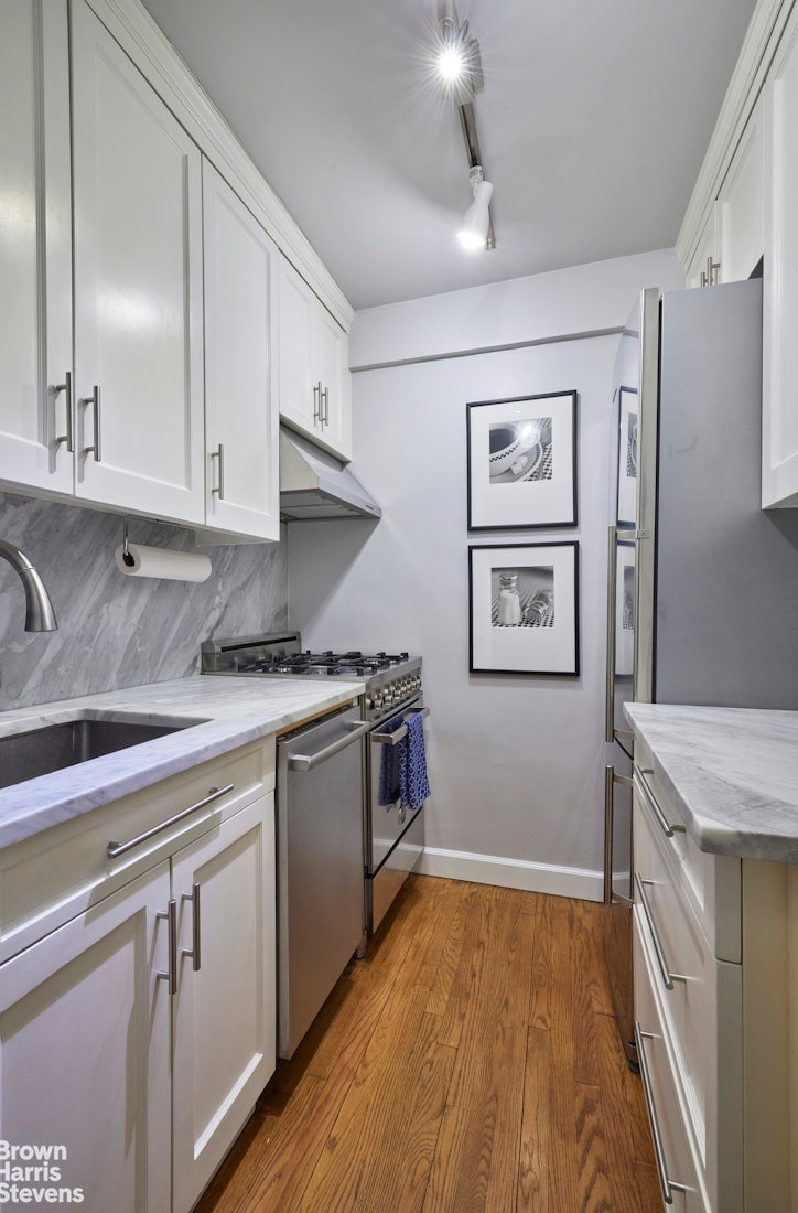 kitchen featuring wood finished floors, a sink, under cabinet range hood, stainless steel appliances, and white cabinetry