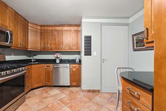 kitchen featuring stainless steel appliances, dark countertops, brown cabinetry, and a sink
