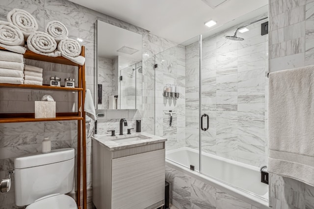 bathroom featuring toilet, enclosed tub / shower combo, tile walls, and vanity