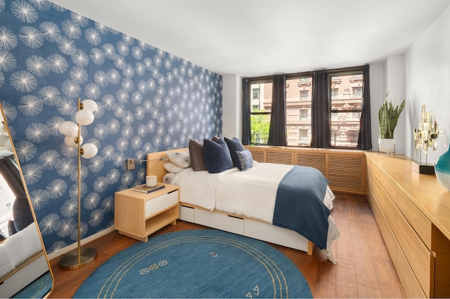 bedroom with baseboards, wallpapered walls, and wood finished floors
