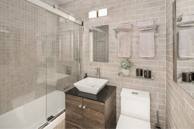 bathroom featuring toilet, tile walls, shower / bath combination with glass door, and vanity