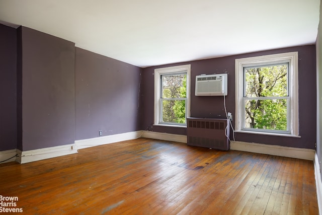 spare room featuring wood-type flooring, a wall mounted air conditioner, plenty of natural light, and radiator heating unit
