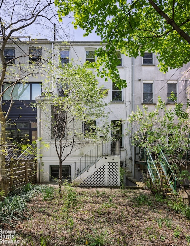 rear view of house with fence, stairs, and stucco siding