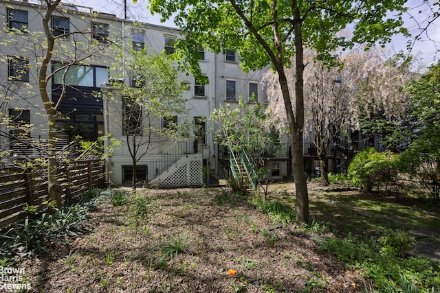 rear view of house with fence, stairs, and stucco siding
