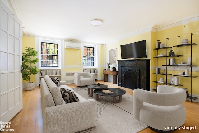 living area with ornamental molding, radiator, wood finished floors, a fireplace, and a wall mounted air conditioner