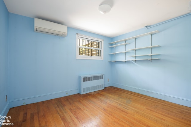 empty room featuring radiator, baseboards, a wall mounted AC, and light wood-type flooring