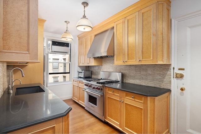 kitchen with designer stove, a sink, wall chimney range hood, light wood finished floors, and dark countertops