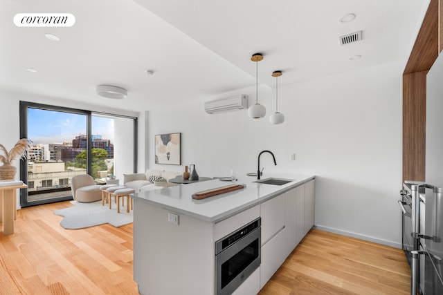 kitchen featuring a peninsula, stainless steel microwave, a wall mounted AC, a sink, and light wood finished floors