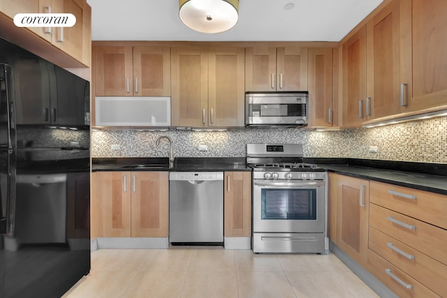 kitchen featuring decorative backsplash, light tile patterned flooring, dark countertops, a sink, and appliances with stainless steel finishes
