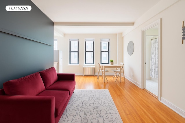 living area featuring baseboards, beam ceiling, radiator heating unit, and light wood finished floors