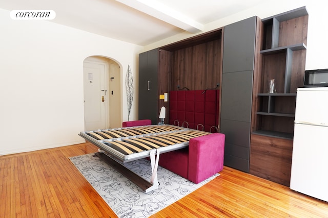interior space featuring visible vents, arched walkways, refrigerator, beamed ceiling, and light wood finished floors