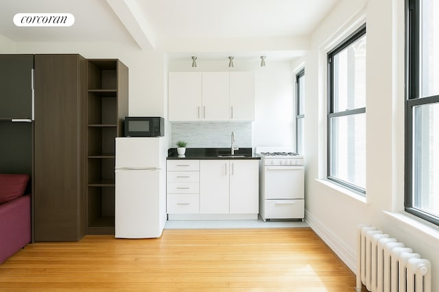 kitchen featuring light wood-style floors, a sink, radiator, and white appliances