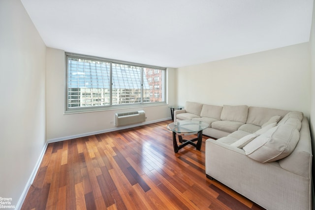 living area with baseboards, a wall unit AC, and wood finished floors