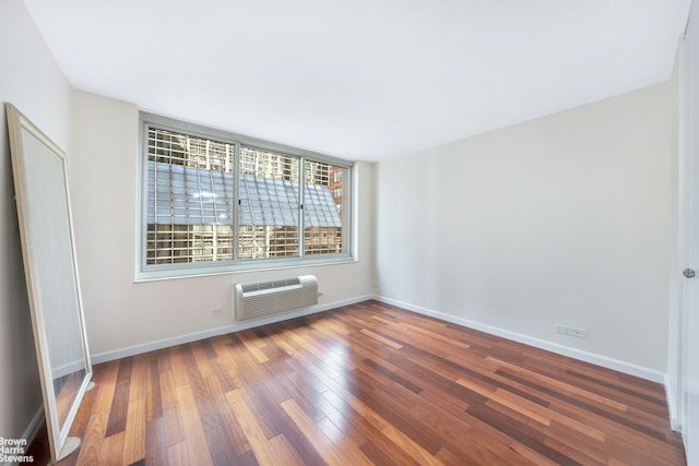 empty room with baseboards, a wall unit AC, and wood finished floors