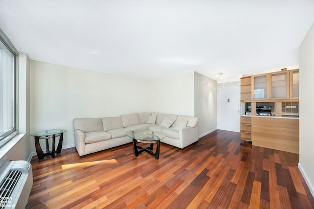 living area featuring baseboards, a wall unit AC, and dark wood-type flooring