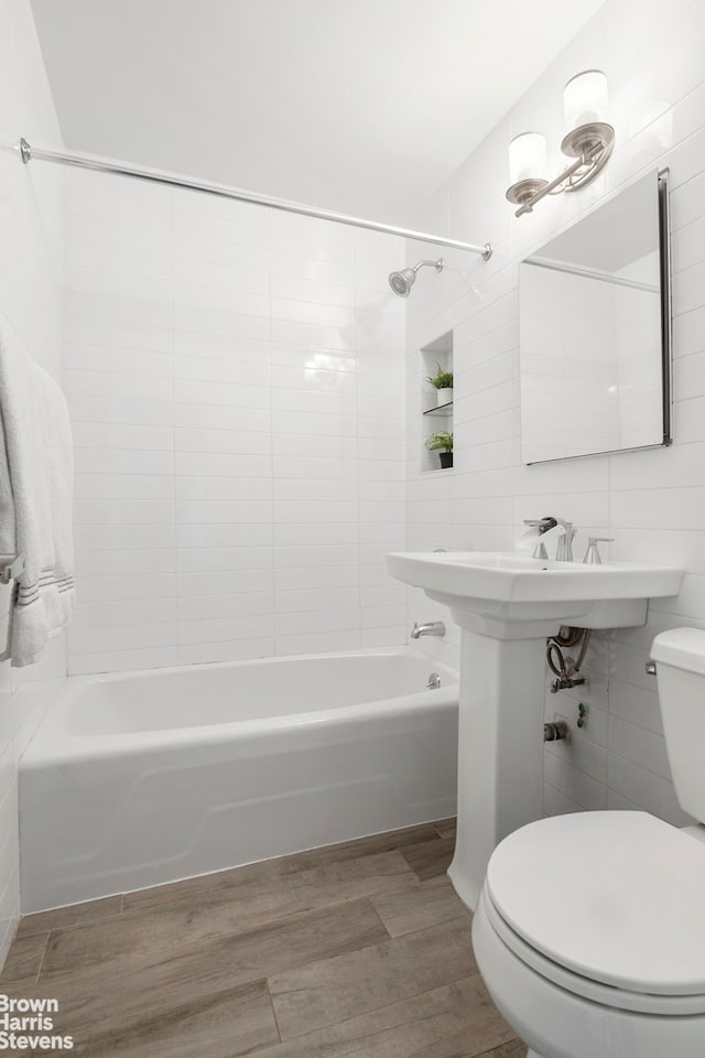 bathroom with toilet, tile walls, shower / tub combination, and wood finished floors