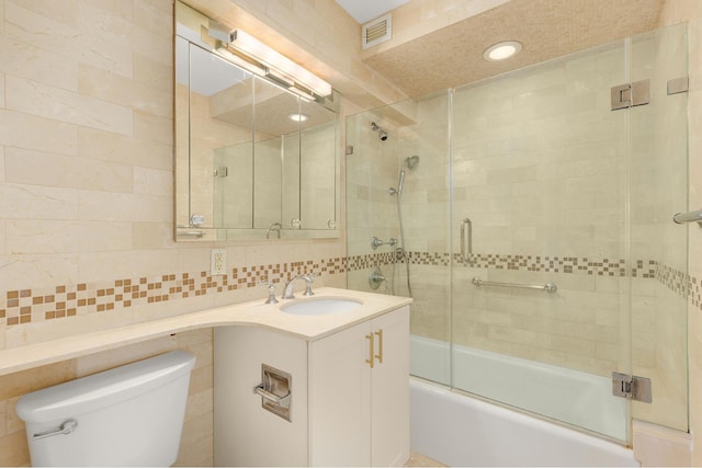 full bathroom featuring visible vents, vanity, toilet, tile walls, and bath / shower combo with glass door