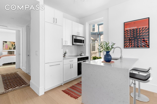1370 Dean St Unit B, New York City, NY 11216 - kitchen featuring appliances with stainless steel finishes, a kitchen bar, light wood finished floors, and white cabinets