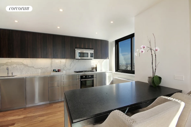 kitchen with appliances with stainless steel finishes, a sink, light wood finished floors, tasteful backsplash, and modern cabinets
