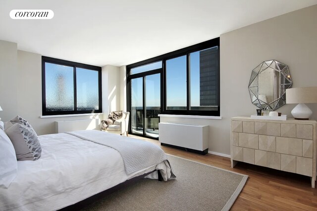 bedroom featuring access to exterior, visible vents, wood finished floors, baseboards, and radiator heating unit
