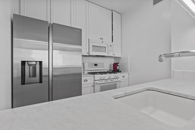 kitchen with white appliances, light stone counters, white cabinetry, and a sink