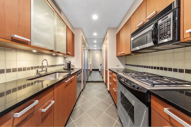 kitchen featuring backsplash, appliances with stainless steel finishes, a sink, dark stone counters, and recessed lighting