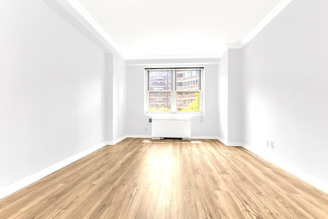 empty room featuring light wood-style floors, radiator, ornamental molding, and baseboards