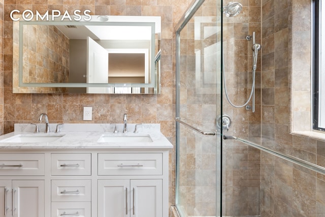 bathroom with a shower stall, double vanity, and tile walls