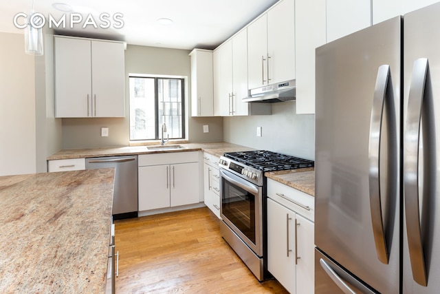 kitchen with stainless steel appliances, under cabinet range hood, a sink, white cabinets, and light wood finished floors