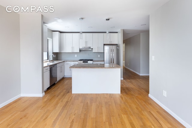 kitchen with appliances with stainless steel finishes, a sink, a kitchen island, white cabinets, and light wood-style flooring