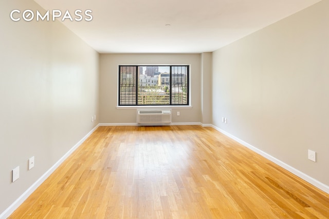 spare room featuring light wood finished floors, a wall mounted AC, and baseboards
