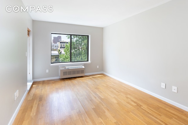 spare room with a wall unit AC, light wood-style flooring, and baseboards