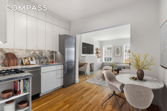 kitchen featuring decorative backsplash, light wood-type flooring, white cabinets, a sink, and stainless steel appliances