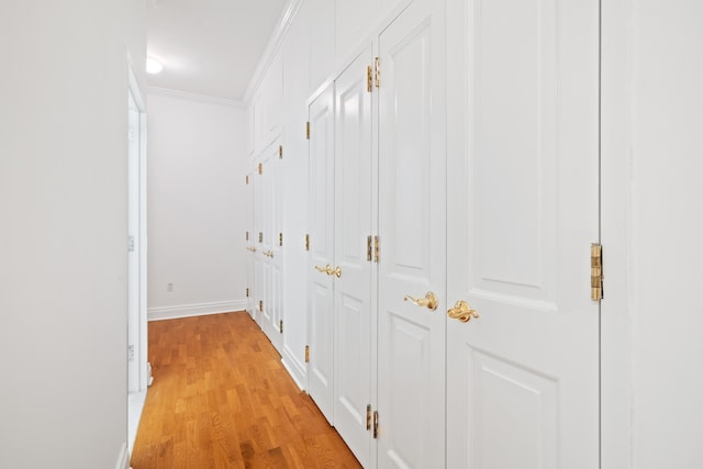 hallway with baseboards, ornamental molding, and light wood finished floors