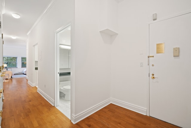 hall with baseboards, ornamental molding, and light wood finished floors