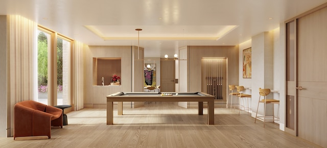 recreation room featuring a tray ceiling, a notable chandelier, and light wood-style flooring